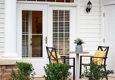 Cozy outdoor patio setup with chairs and a table against a white wall.