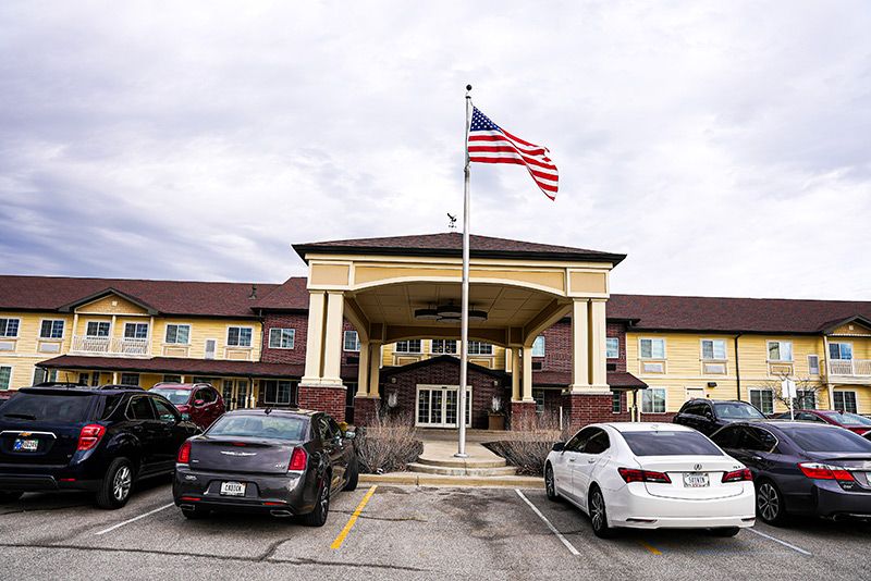 A hotel entrance with an American flag flying above and cars parked in the lot.