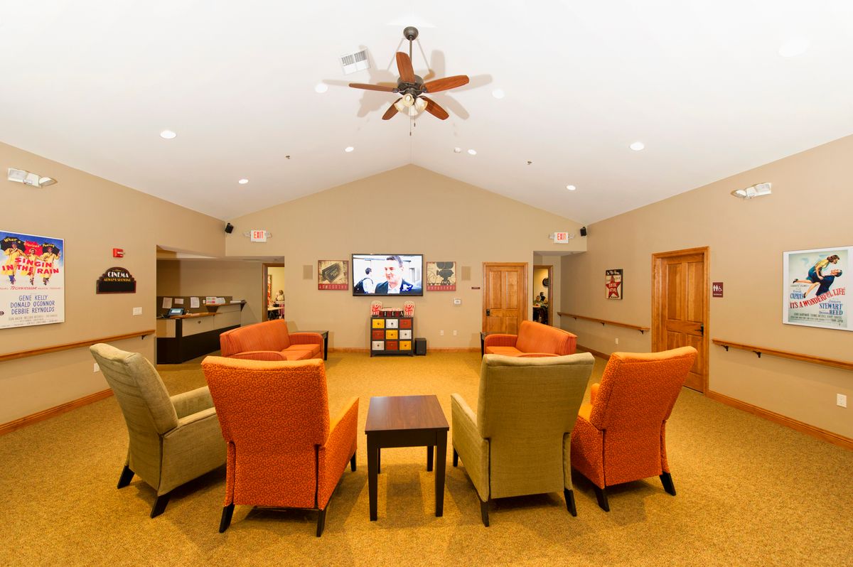 A cozy living room with colorful armchairs arranged facing a television, under a ceiling fan.