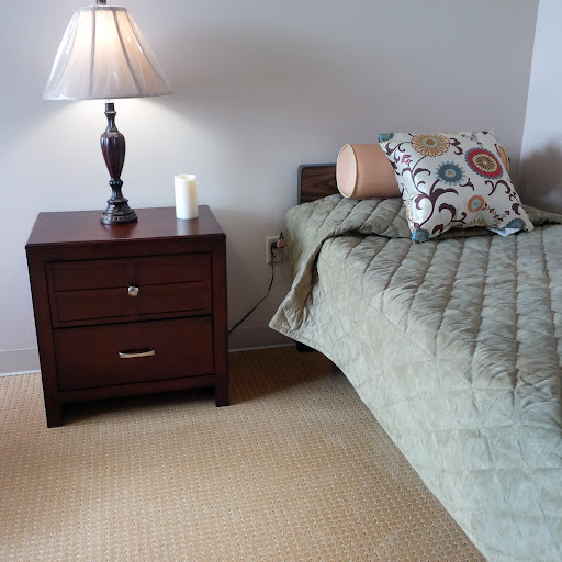 A cozy bedroom setup featuring a neatly made bed with a green quilt, a nightstand with a lamp, and decorative elements.