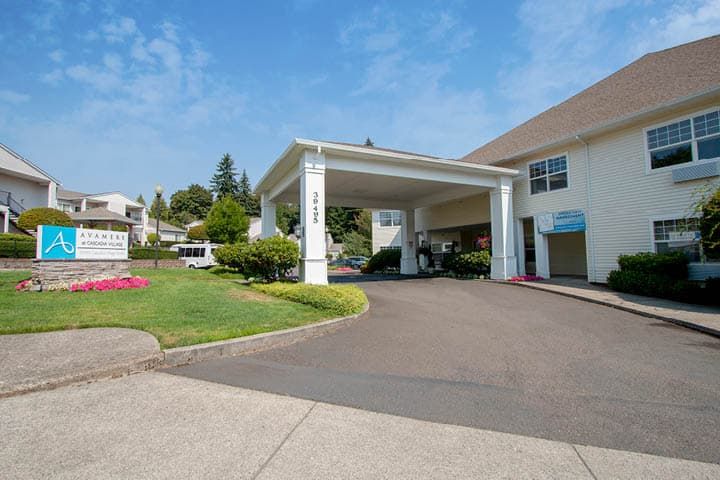 A building with a covered entrance and landscaped surroundings on a sunny day.