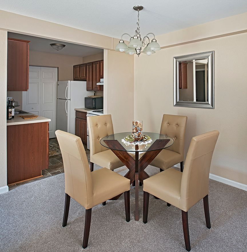 A cozy dining area with a round table and four upholstered chairs, accompanied by a chandelier and adjacent to the kitchen.