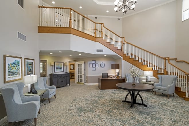 A well-lit lobby with a grand staircase, seating area, and chandelier.