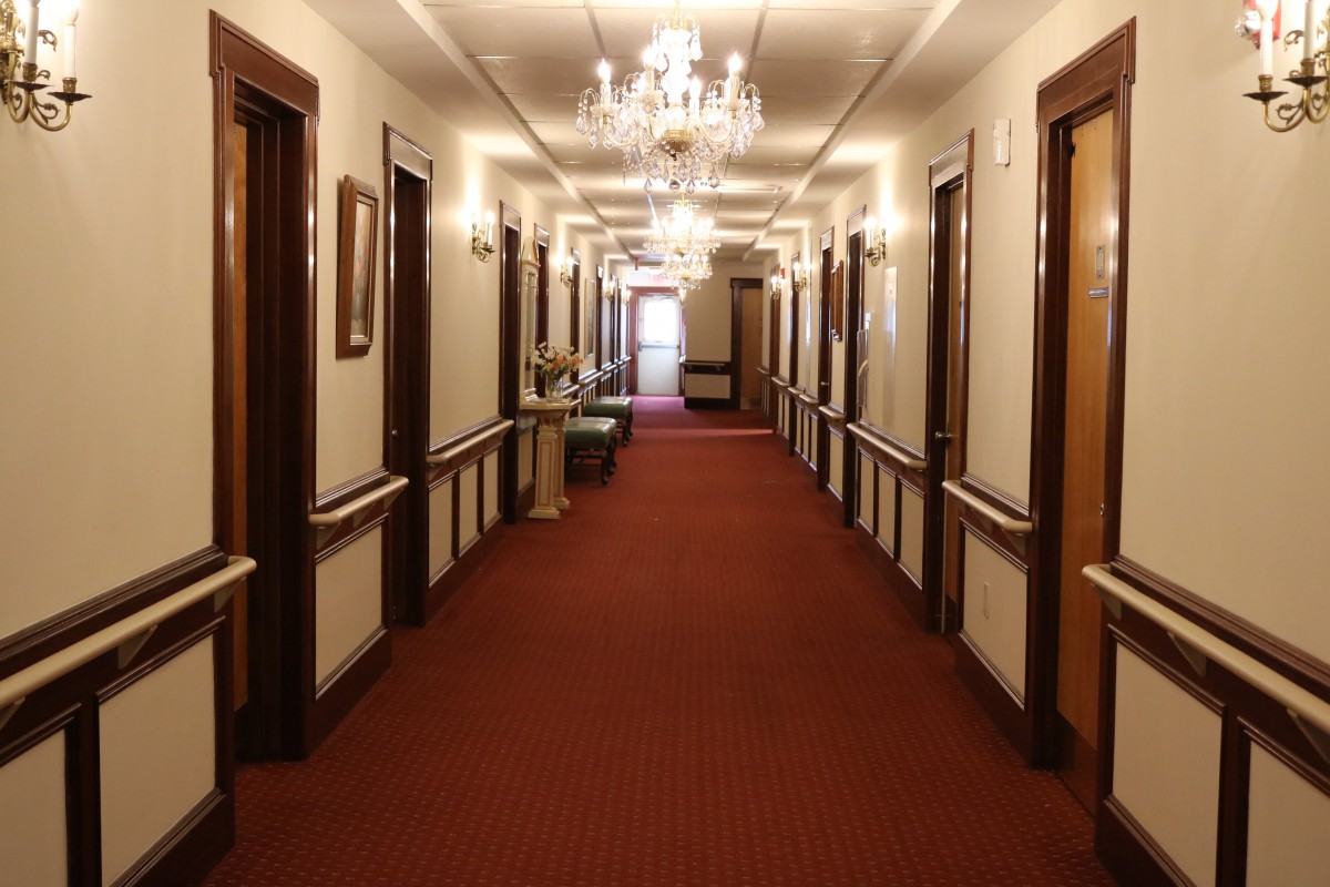 A luxurious hotel hallway with chandeliers and a red carpeted floor.