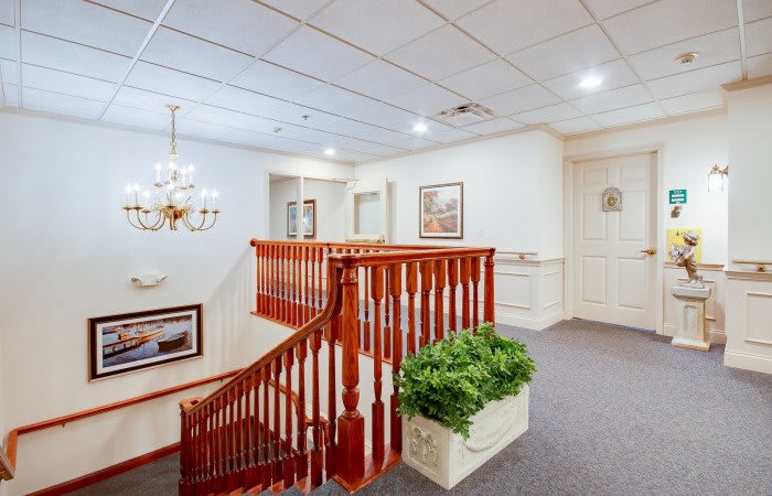 A hallway interior with a wooden staircase and decorative elements, including paintings and a chandelier.