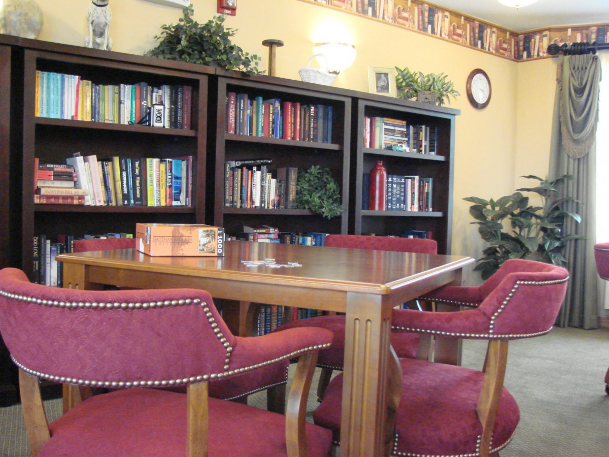 A cozy reading area with bookshelves, a wooden table, and red chairs.
