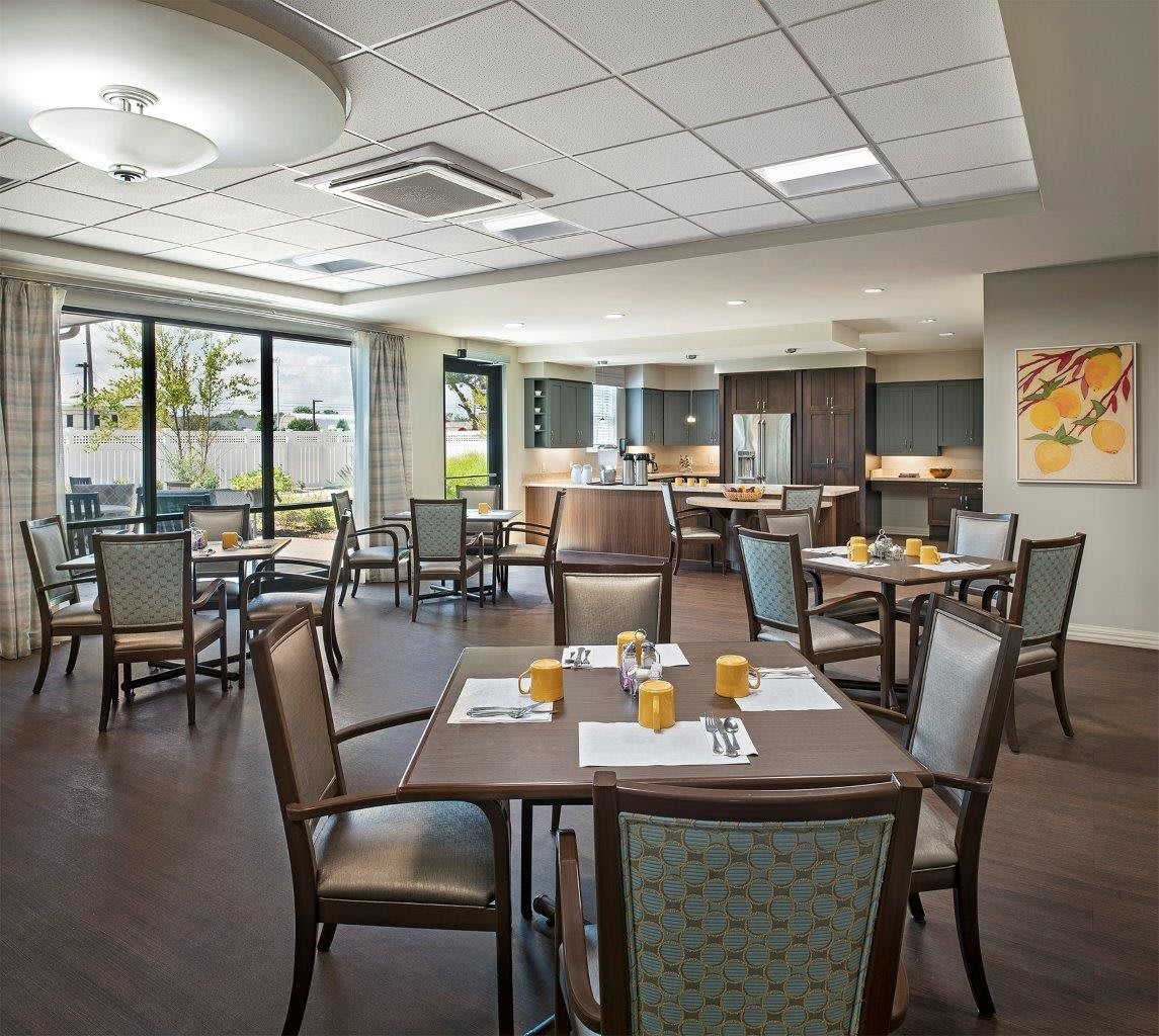 A modern dining room with neatly arranged tables and chairs, featuring ample natural light from large windows.