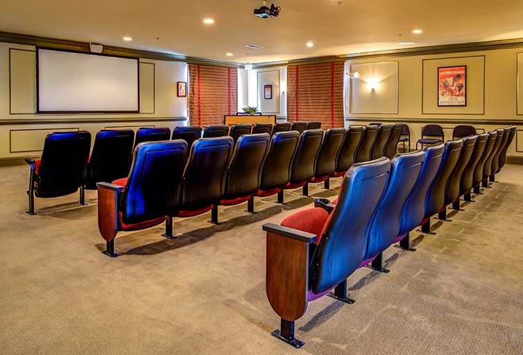 An empty theater-style conference room with arranged seating and a projector screen.