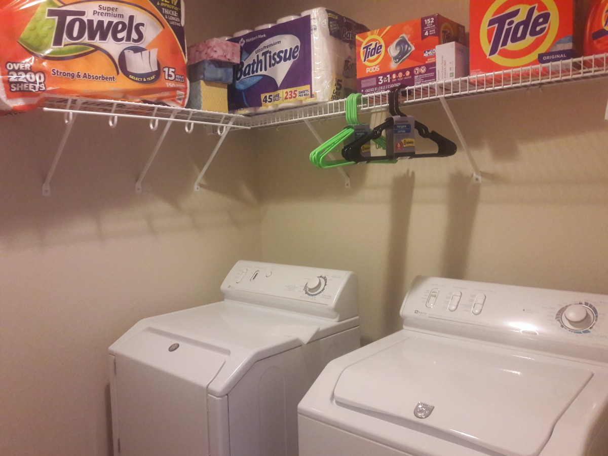A laundry room with a washing machine and dryer, stocked with detergent and other laundry supplies on the shelves.