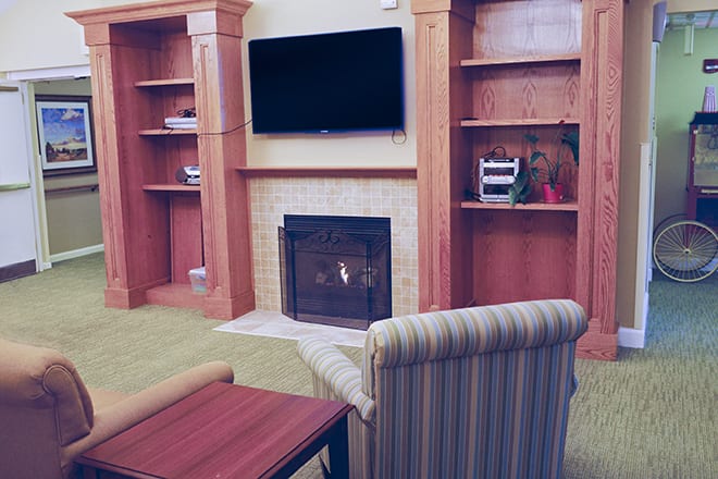 A cozy living room setup featuring a fireplace, flat-screen TV mounted above, and built-in wooden shelves.