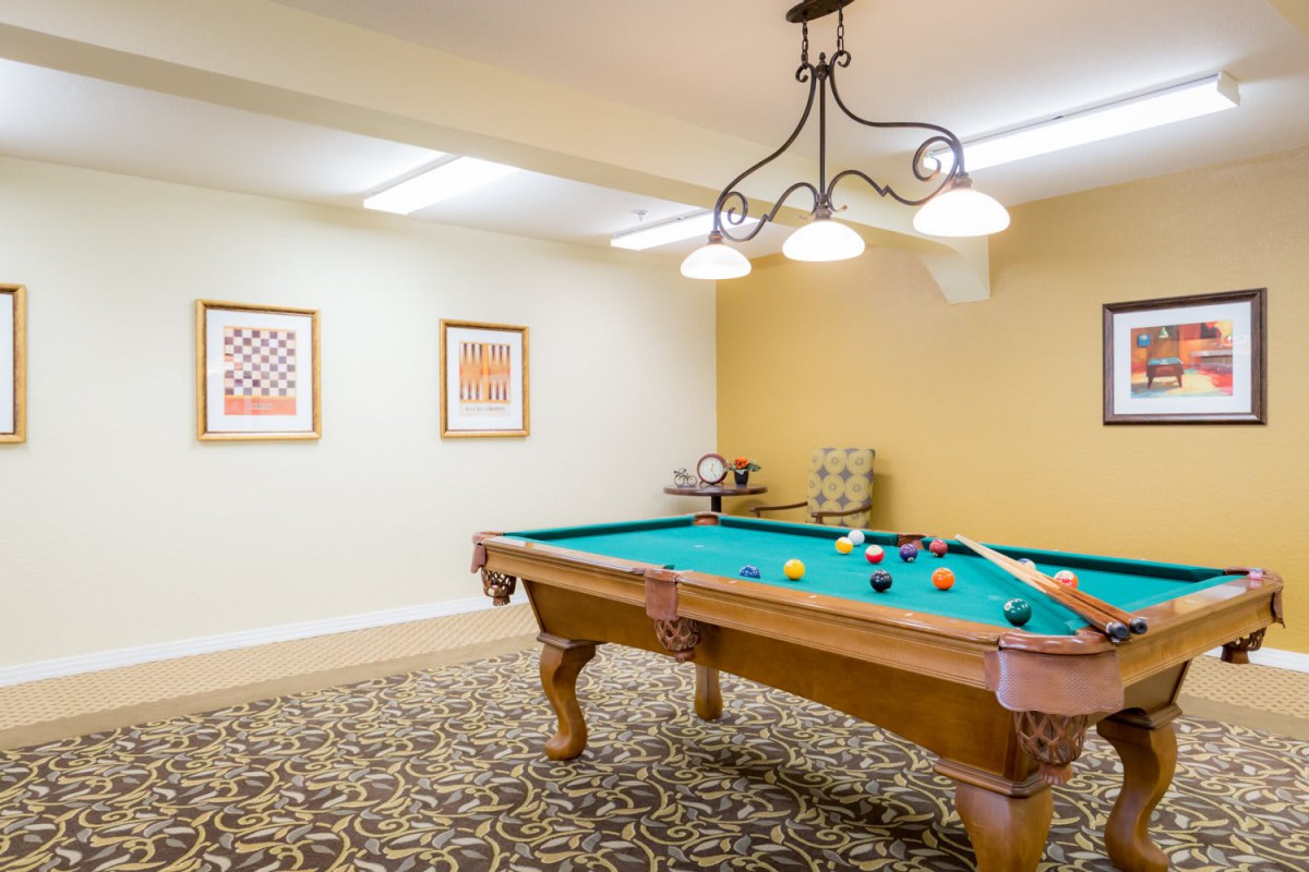 A well-lit pool room with a billiard table and decorative artwork on the walls.