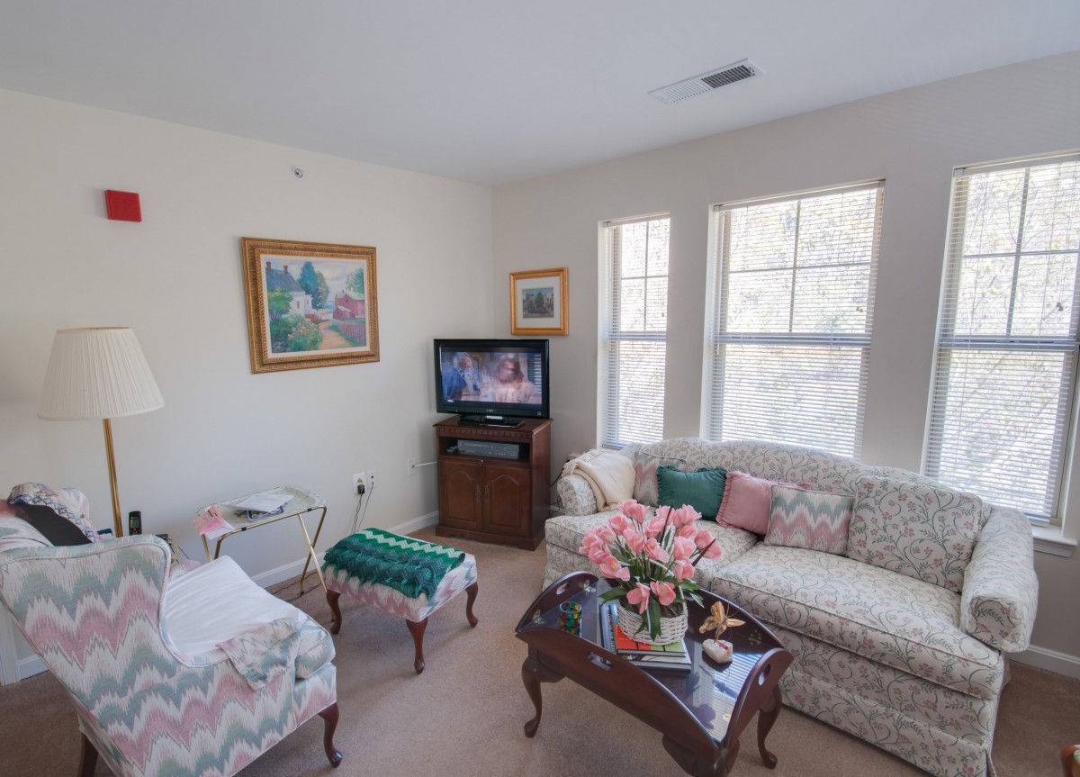 A cozy living room with a sofa, chairs, a coffee table adorned with flowers, and a television.