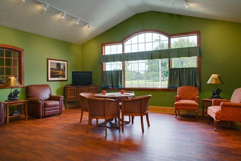 A spacious living room with green walls, large windows, and comfortable seating around a central table.