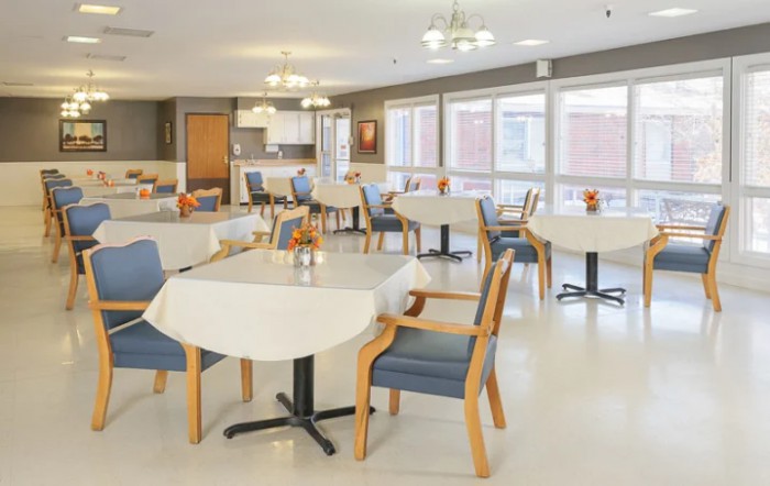A bright and spacious dining area with neatly arranged tables and chairs, featuring large windows and overhead lighting.