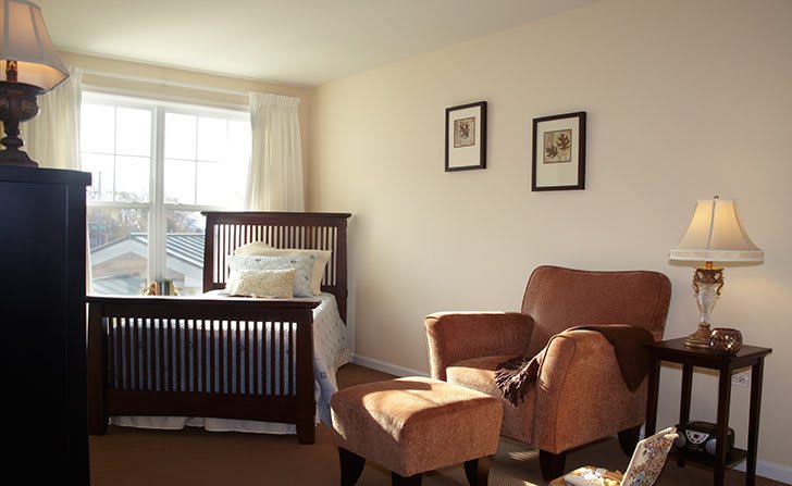 A cozy bedroom with an armchair and a neatly made bed by the window.
