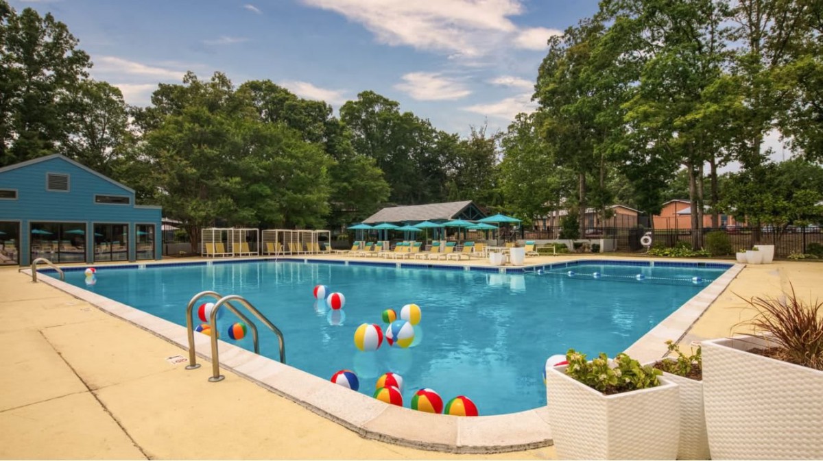 An inviting swimming pool surrounded by trees, with colorful beach balls floating on the surface under a sunny sky.