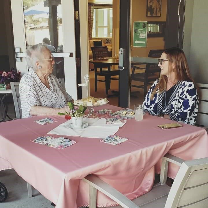 An elderly person and a woman enjoying a conversation at an outdoor dining table.