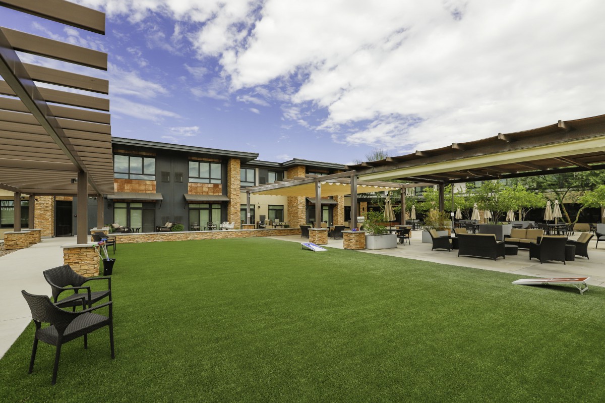 A modern building with a spacious grass lawn and outdoor seating area beneath a cloudy sky.