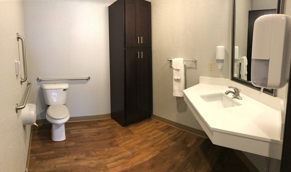 A modern bathroom with accessibility features, including a toilet, sink, cabinet, and wooden flooring.