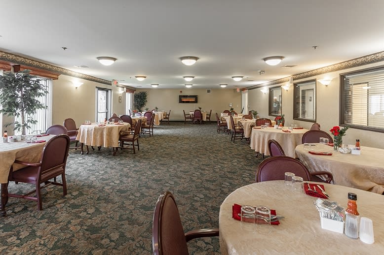 A spacious banquet hall with round tables and chairs arranged neatly, featuring a carpeted floor and ceiling lights.
