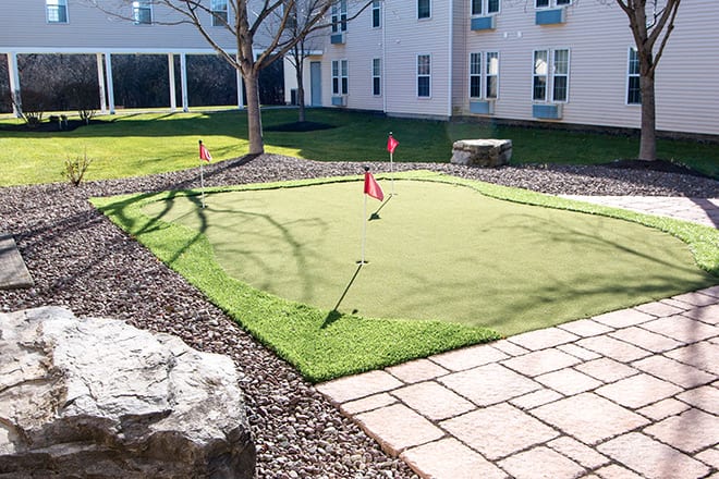 An outdoor putting green surrounded by a landscaped area, ready for golf practice.