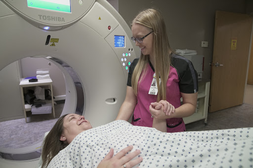 A nurse assists a patient preparing for a CT scan in a hospital setting.