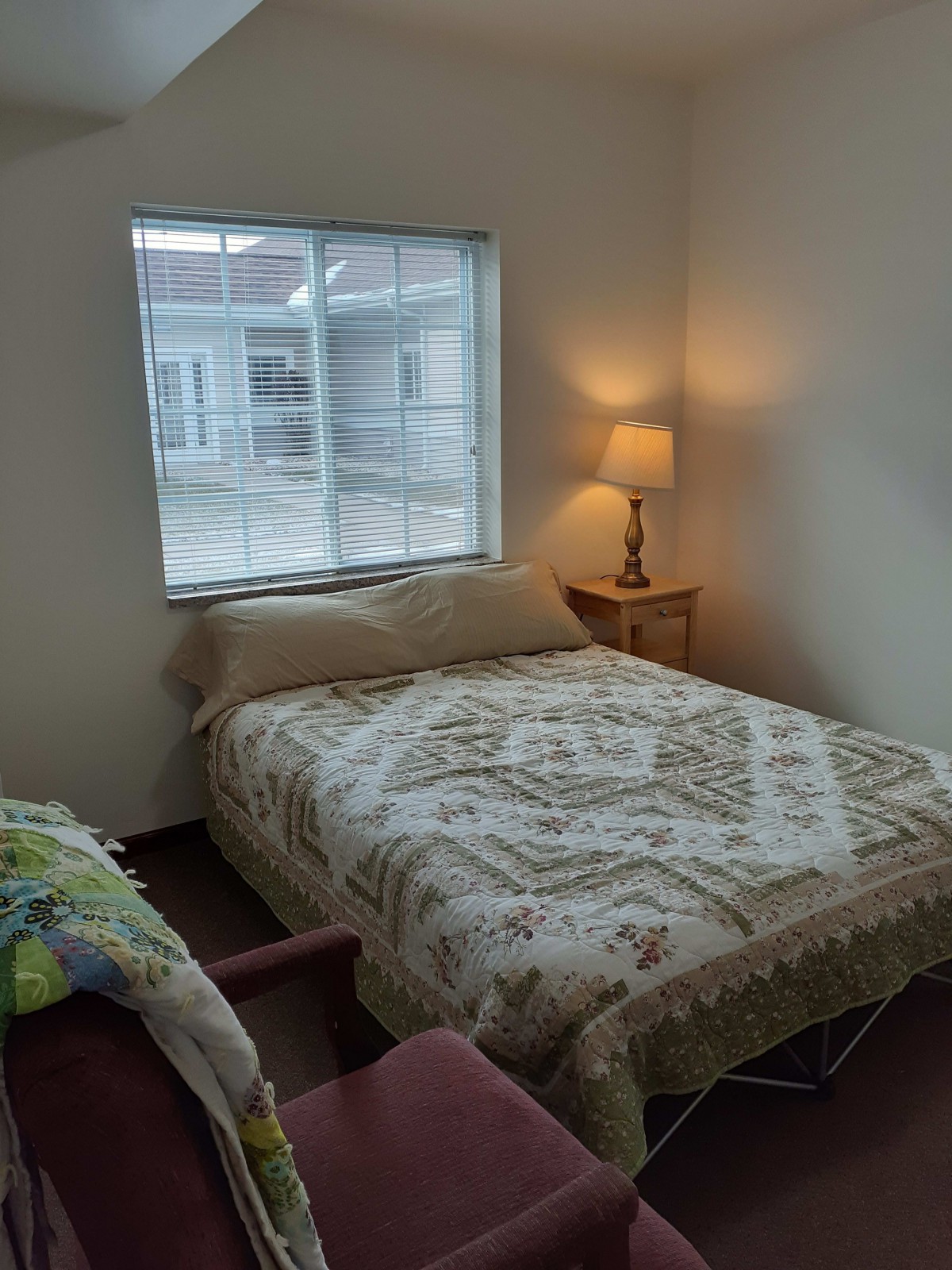 Cozy bedroom with a patterned bedspread and a warm lamp by the window.