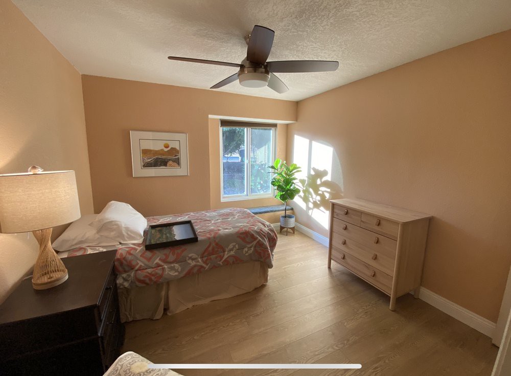 A cozy bedroom with a single bed, dresser, and natural light from a large window.