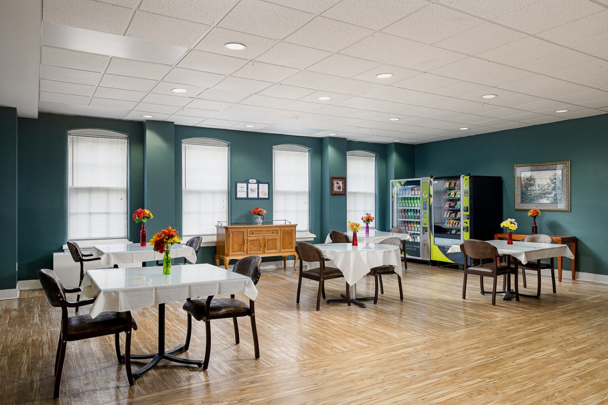 A well-lit dining area with tables, chairs, and vending machines against blue walls.