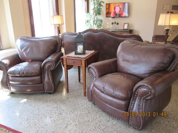 A cozy living room with leather armchairs and a sofa, accompanied by a small wooden table and a lamp.