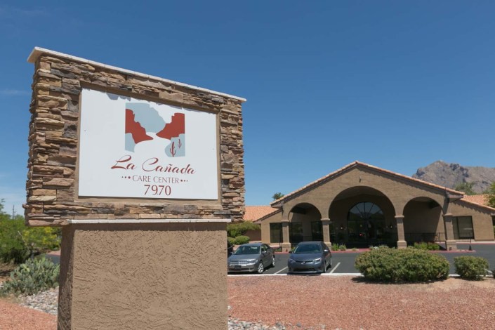 A photo of a building with a stone sign reading 'Los Robles Apartments' and a parking lot in front.