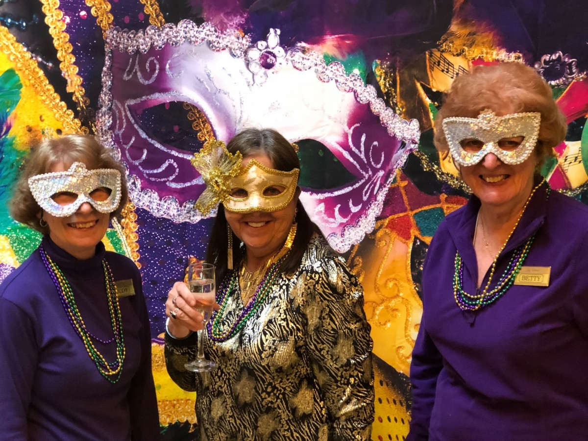 Three women wearing festive masks and costumes at a masquerade party.