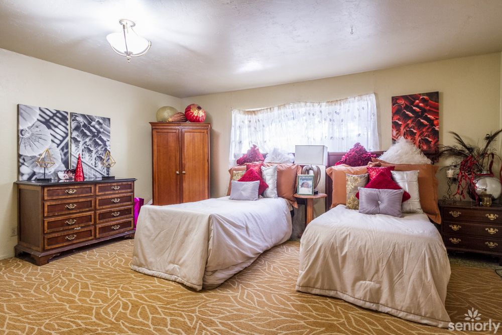 A cozy bedroom featuring twin beds with decorative pillows, wooden furniture, and a carpeted floor.
