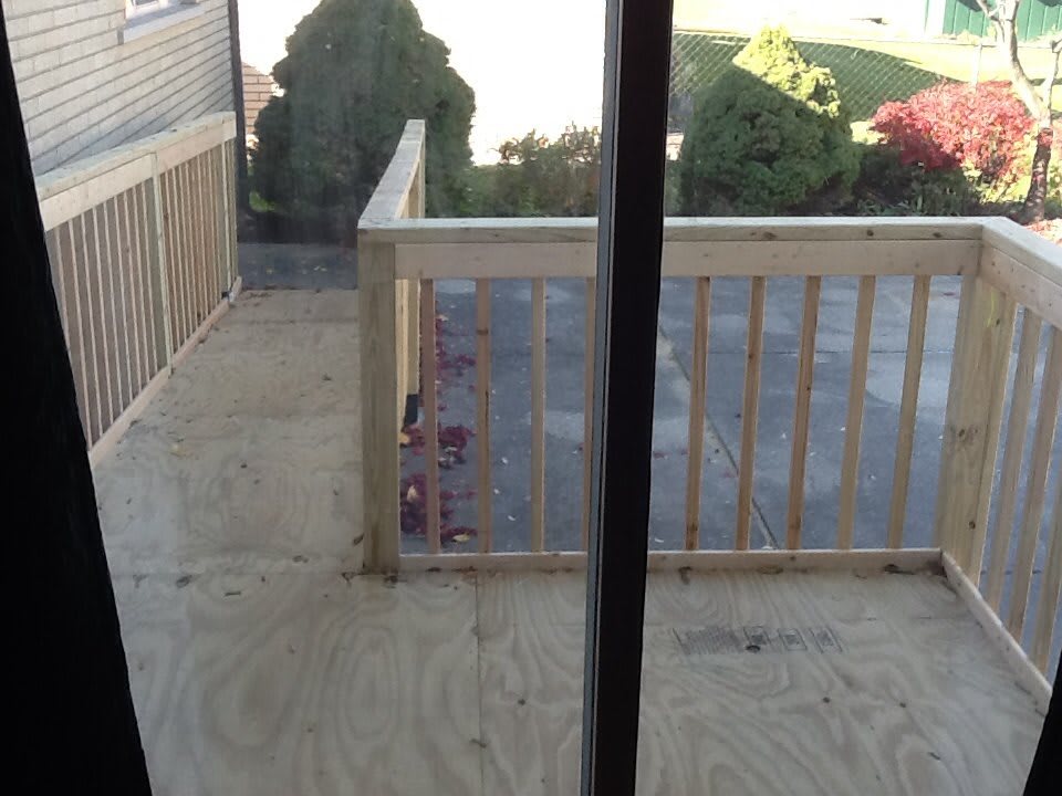 A newly constructed wooden balcony viewed through a glass door.