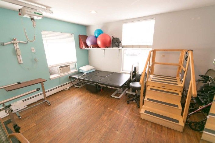 A rehabilitation room equipped with a therapy bed, stairs, and exercise balls.