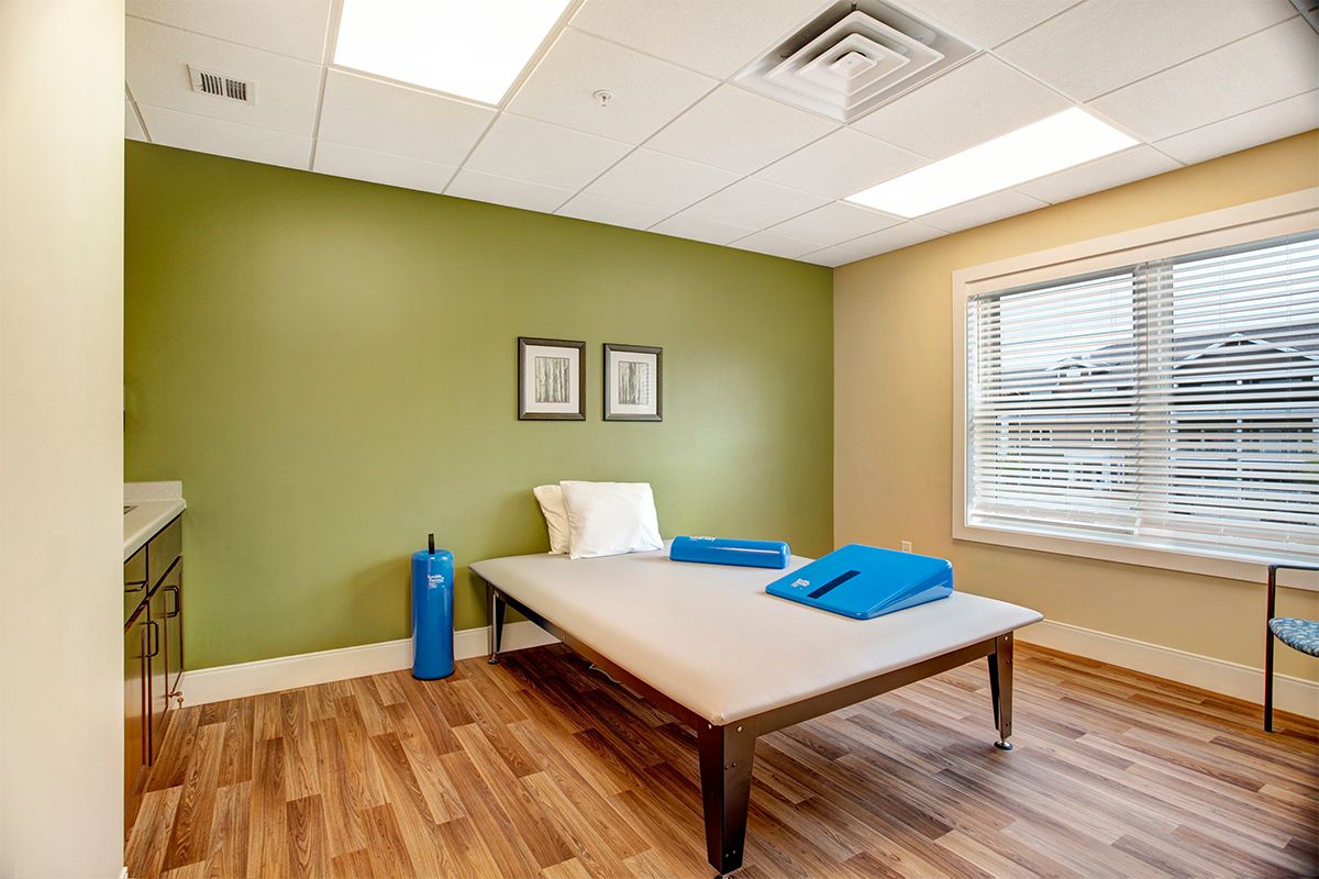 A serene therapy room with a massage table, showcasing calming green walls and wood flooring.