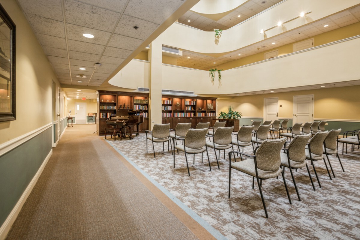 A spacious library interior with rows of chairs and bookshelves, featuring a well-lit open area.