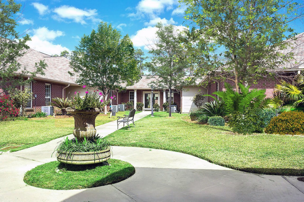 A peaceful garden area with a building in the background, featuring trees, a bench, and a clear sky.
