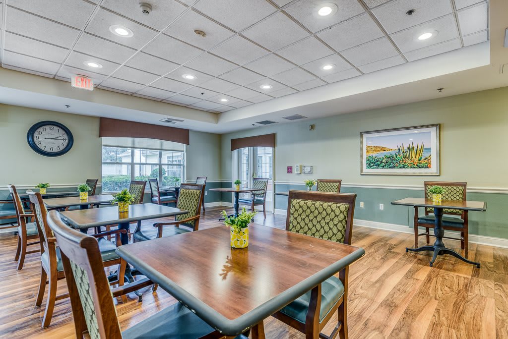 A well-lit dining area with neatly arranged tables and chairs, decorated with potted plants.