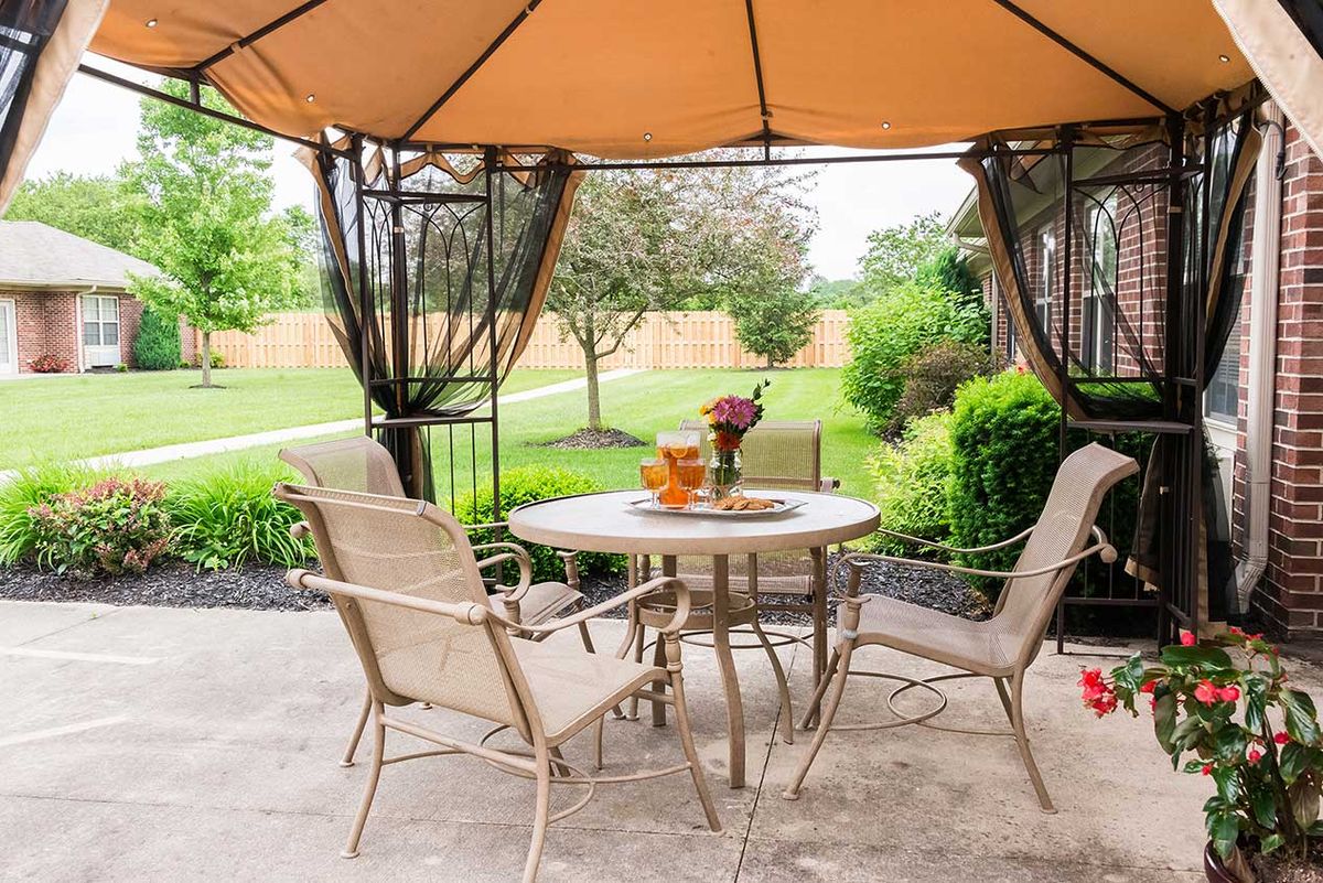 A cozy outdoor patio with a gazebo and dining set in a lush backyard setting.