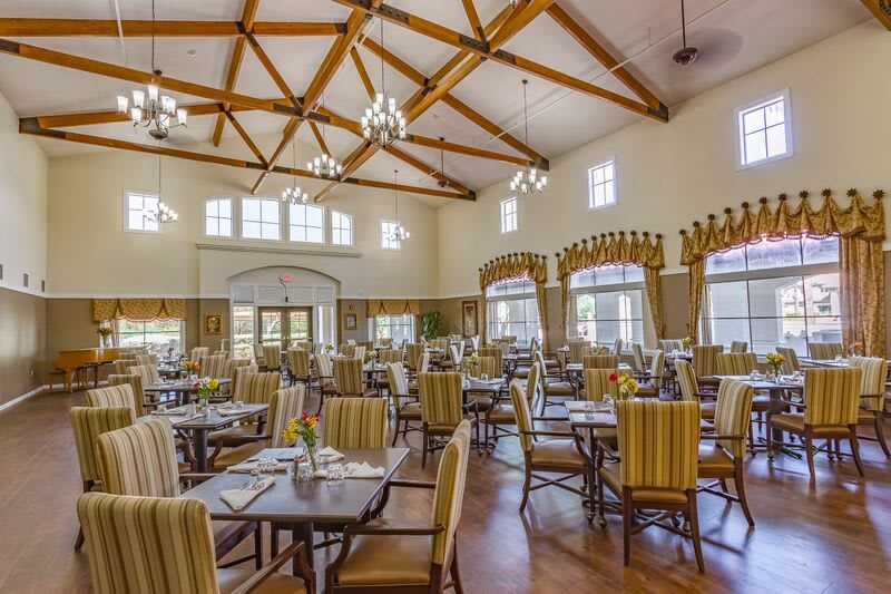 A spacious dining room with elegant chandeliers and neatly arranged tables and chairs.