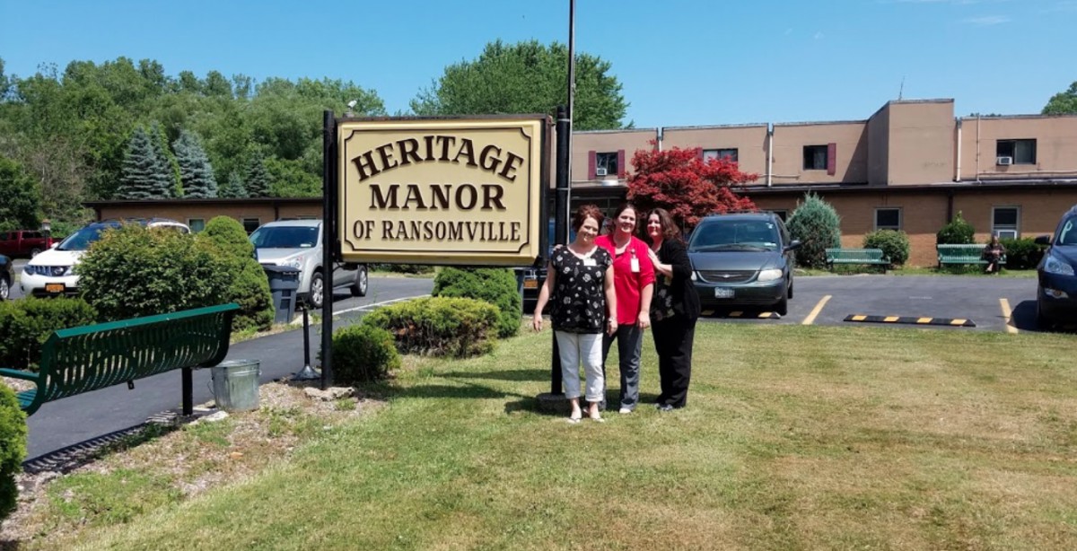 A group of people standing in front of the Heritage Manor of Ransomville sign.