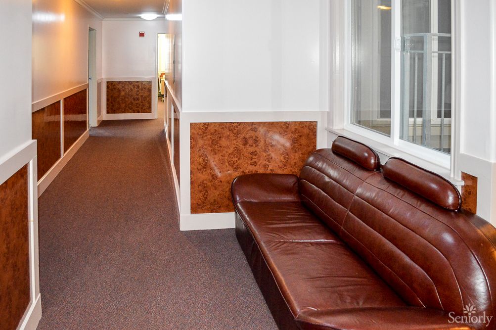 A hallway with a brown leather sofa and carpeted floor.