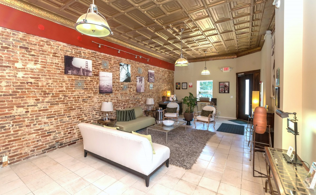 A stylish living room interior featuring a white sofa, brick walls adorned with artwork, and modern ceiling lights.
