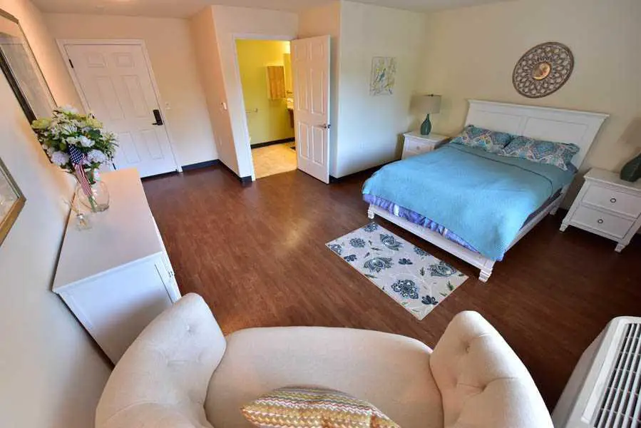 A cozy bedroom with wooden flooring, featuring a bed, armchair, and stylish decor.