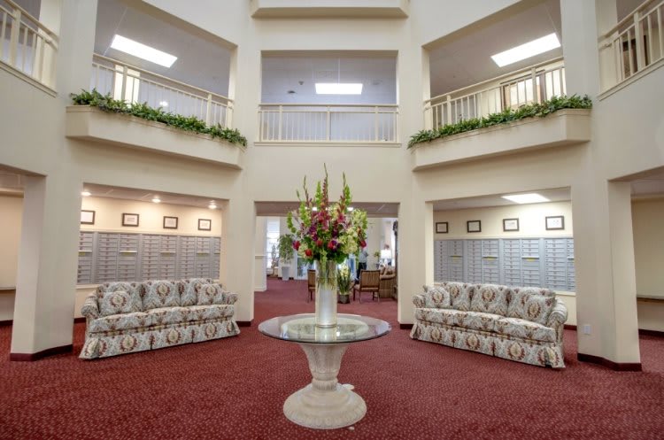 A spacious lobby featuring elegant sofas, a central floral arrangement on a glass table, and an open balcony layout.