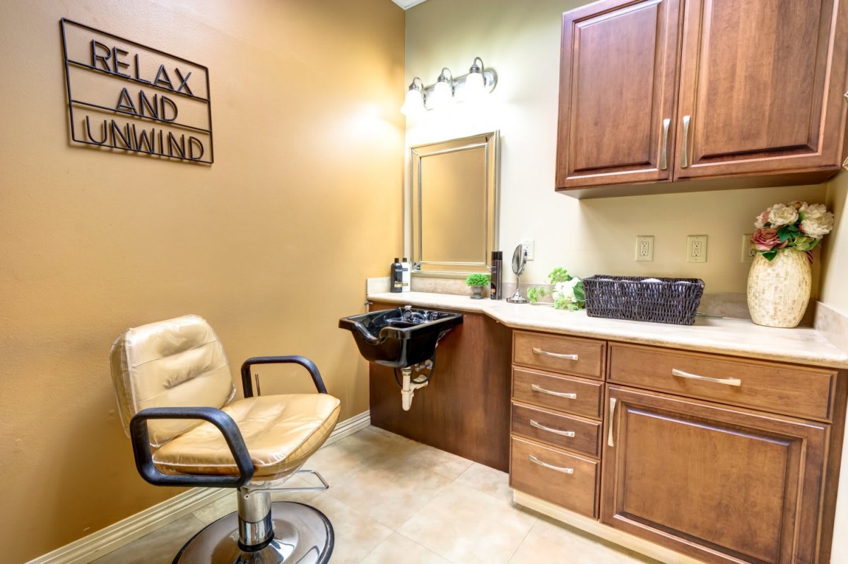A cozy salon interior featuring a hairdressing chair, sink, mirror, and cabinetry.