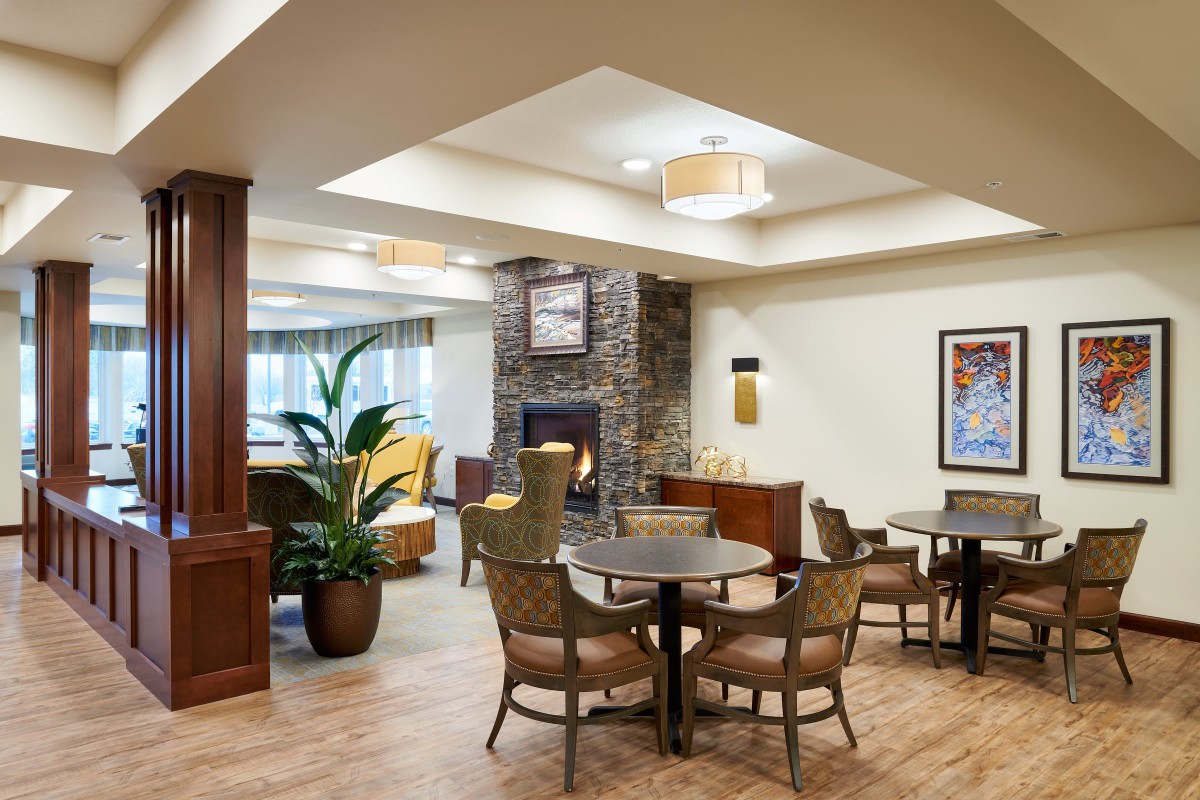 A cozy lounge area featuring a central fireplace, with several chairs and tables arranged for comfort.