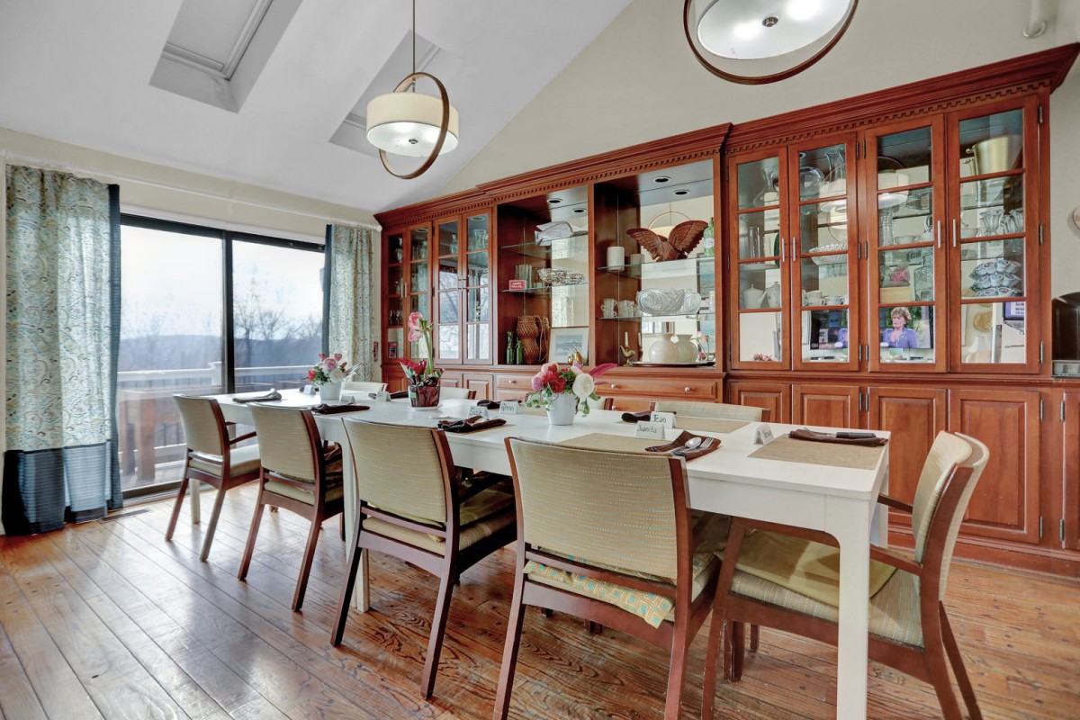 A well-appointed dining room with a large table, elegant chairs, and a wooden cabinet displaying glassware.