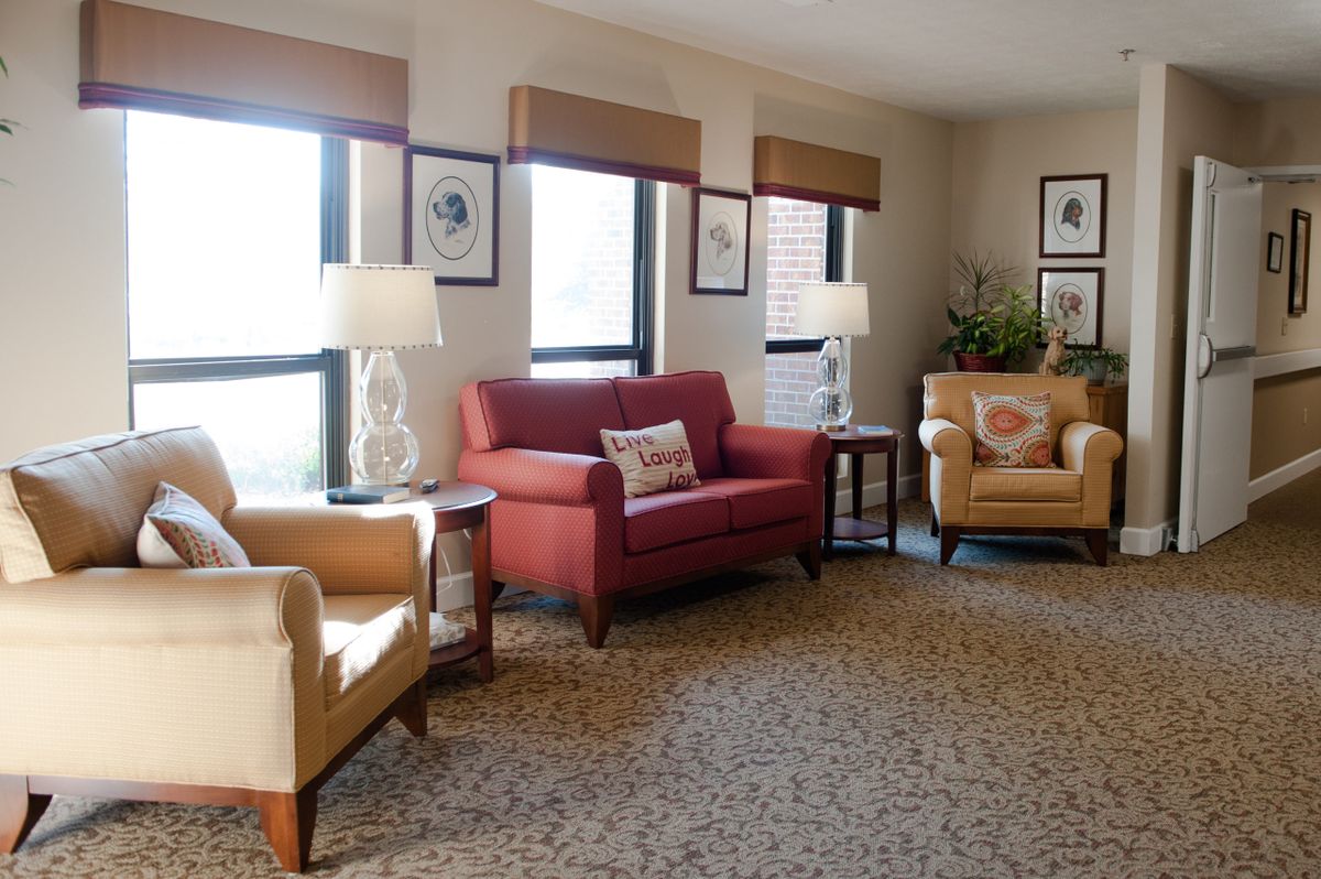 A cozy living room with sofas and armchairs, decorated with lamps and wall art.